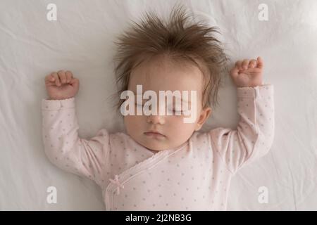 Friedliches, verlähtes Mädchen, das auf einem hellen, sauberen Leinenlaken liegt Stockfoto