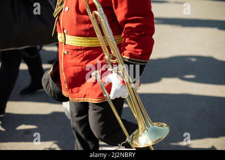 Orchestermitglied hält Messingpfeife. Details zum Trompeter. Zeremonielle rote Uniform. Militärkapelle auf der Straße. Stockfoto