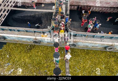 Dhaka, Bangladesch. 03. April 2022. Eine Reihe von Arbeitern, die bis zu 200 Ladungen pro Tag transportieren, entladen eine frische Ladung, indem sie die schweren Lasten der Kohle in Körben tragen, die prekär auf ihren Köpfen im Gabtoli Coal Field, Dhaka, Bangladesch, balanciert werden. Sehr früh am Morgen beginnen die Arbeiter bis zum Sonnenuntergang mit dem Entladen von Kohle, sie verdienen etwa $7 pro Tag. Es gibt keine speziellen Schuhe an ihren Füßen und keine Handschuhe in ihren Händen, um Kohle von Frachtschiffen zu entladen. Kredit: ZUMA Press, Inc./Alamy Live Nachrichten Stockfoto