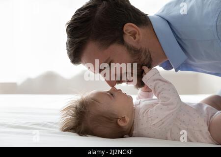 Glücklicher Vater beruhigendes, beruhigendes Baby, das auf dem Rücken im Bett ruht Stockfoto