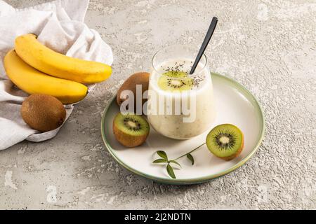 Energy Fruit Smoothie aus Bananen und Kiwi in einem Glas auf einer Keramikplatte und einem konkreten Hintergrund mit Früchten. Das Konzept der gesunden Ernährung Stockfoto