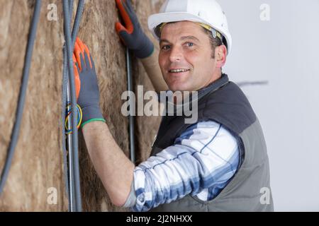 Arbeiter in Schutzhandschuhen, die eine Wollwand isolieren Stockfoto