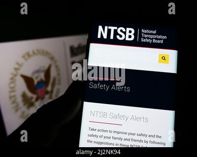 Person, die das Smartphone mit der Webseite des US National Transportation Safety Board (NTSB) auf dem Bildschirm vor dem Siegel hält. Konzentrieren Sie sich auf die Mitte des Telefondisplays. Stockfoto