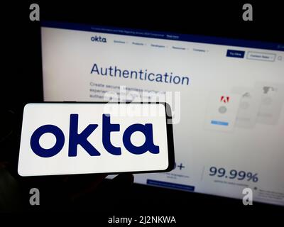 Person, die Mobiltelefon mit dem Logo des US-amerikanischen Identitätsmanagementunternehmens Okta Inc. Auf dem Bildschirm vor der Business-Webseite hält. Konzentrieren Sie sich auf die Telefonanzeige. Stockfoto