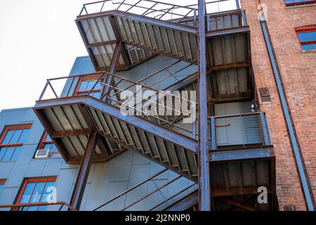 Blick auf eine Holztreppe auf der Außenseite eines roten Backsteingebäudes, die zu verschiedenen Ebenen einer Wohnung oder eines Unternehmens führt Stockfoto