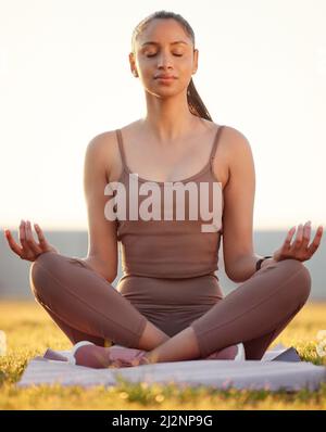 Sie genießt ihre Zeit in einem Zen-Garten. Aufnahme einer sportlichen jungen Frau, die beim Training im Freien meditiert. Stockfoto