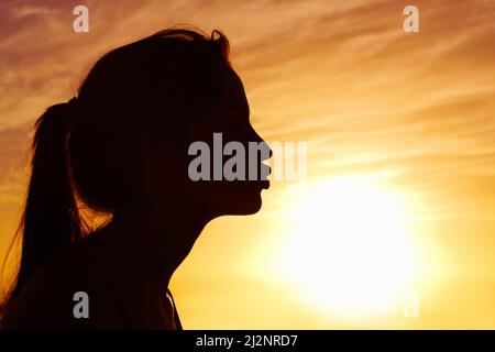 Nahaufnahme einer Frau, die die Sonne gegen den schönen Himmel küsst. Profilansicht einer Frau, die die Sonne gegen den schönen Himmel küsst. Stockfoto