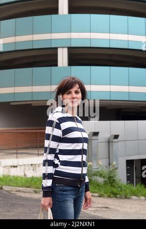 Eine Erwachsene Frau in einem gestreiften Pullover vor dem Stadtgebäude im Hintergrund. Stockfoto