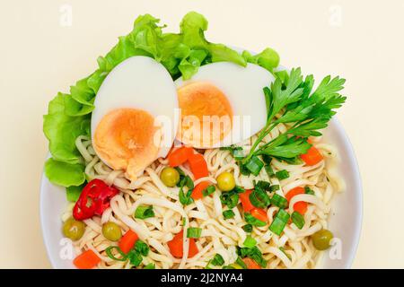 Schönes Nudelgericht mit grüner Erbse, Karotten, Eiern, rotem heißen Pfeffer und Grüns auf weißem Hintergrund. Instant Nudeln mit Gemüse Stockfoto