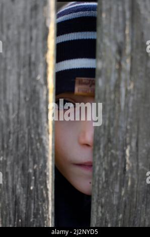 Junge schaut durch eine Lücke im Zaun Stockfoto
