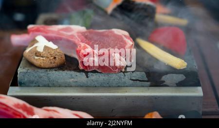 Gegrillte Rindersteaks mit Gewürzen auf HOT Stone mischen. Asiatisches Dinner-Konzept. Dampfendes heißes Steak auf heißem Stein. Stockfoto