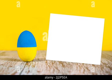 Frohe Ostern mit einem Ei in den Farben der Ukraine gemalt. Grußkarte für ein Ostern voller Liebe und Frieden. Platz für Ihre Nachricht kopieren. Stockfoto