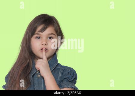 Nettes gebräuntes langhaariges kleines Mädchen, das Finger auf die Lippen setzt und shh sagt. Isoliert. Stockfoto