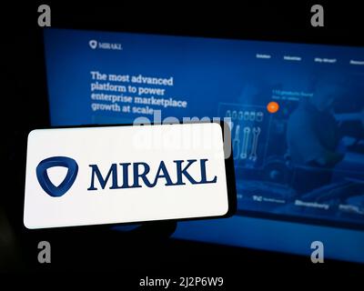 Person, die ein Mobiltelefon mit dem Logo des französischen E-Commerce-Softwareunternehmens Mirakl auf dem Bildschirm vor der Business-Webseite hält. Konzentrieren Sie sich auf die Telefonanzeige. Stockfoto