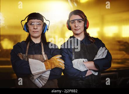 Waren zuversichtlich, dass wir schaffen können. Beschnittenes Porträt zweier attraktiver junger Kunsthandwerkerinnen, die mit gekreuzten Armen in ihrer Werkstatt stehen. Stockfoto