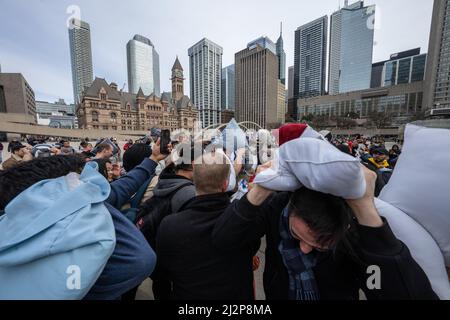 Toronto, Kanada. 02. April 2022. Menschen benutzen Kissen, um sich während eines gemeinschaftlichen Kissenkampfes gegenseitig zu treffen. Dutzende von Menschen mit Kissen versammelten sich auf dem Nathan Philips Square, um den Internationalen Pillow Fight Day in Toronto, Kanada, zu feiern, der jedes Jahr am ersten Samstag im April stattfindet. Das globale Ereignis wurde erstmals 2008 gefeiert. (Foto von Katherine Cheng/SOPA Images/Sipa USA) Quelle: SIPA USA/Alamy Live News Stockfoto