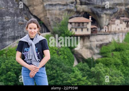 Meteora, Griechenland - 29. Mai 2021: Mädchen-Touristin wird vor der Kulisse des Klosters in den Bergen fotografiert. Spitze des Meteora-Tals. Stockfoto