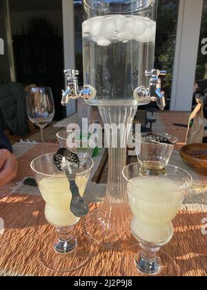 Absinth-Brunnen mit Wasser und Eiswürfel und vier Gläsern und Löffel. Feiern Sie im Freien bei Sonnenschein. Stockfoto