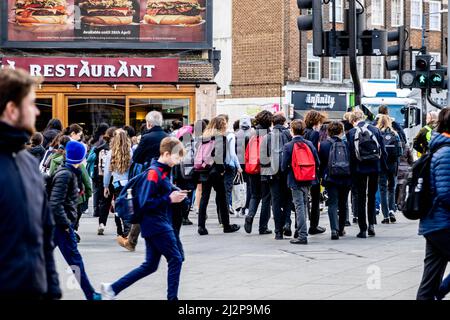 Kingston upon Thames London, Großbritannien, 01 2022. April, Gruppen- oder Schulenkinder warten darauf, an der Ampel eine belebte Hauptstraße im Stadtzentrum zu überqueren Stockfoto