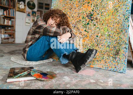 Lächelnd junge weiße rothaarige Frau Künstler Gemälde sitzt vor der Leinwand in Studio-Werkstatt Stockfoto