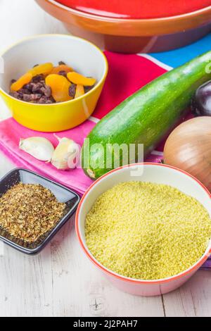 Marokkanischer Couscous mit Gemüse, Gewürzen und getrockneten Früchten auf einem bunten Tischtuch Stockfoto