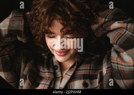 Lächelnde junge Rothaarige Frau im karierten Hemd, die im Studio posiert Stockfoto