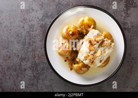 Kabeljaufilet in Olivenöl mit Knoblauch gebacken, serviert mit Kartoffeln aus der Nähe auf einem Teller auf dem Tisch. Horizontale Ansicht von oben Stockfoto