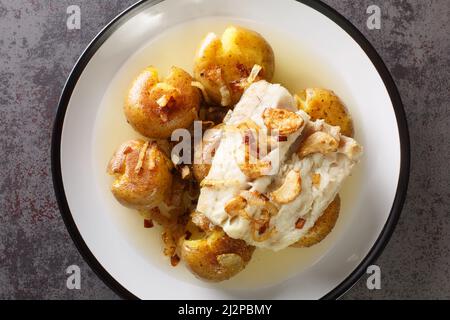 Traditioneller Bacalhau a Lagareiro Gegrillter gesalzener Kabeljau mit Olivenöl serviert mit gebackenen Kartoffeln in der Nähe auf dem Teller auf dem Tisch. Horizontale Draufsicht f Stockfoto