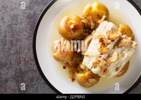 Portugiesischer Bacalhau a Lagareiro gesalzener Kabeljau in Öl gebacken mit Kartoffeln aus der Nähe auf einem Teller auf dem Tisch. Horizontale Ansicht von oben Stockfoto