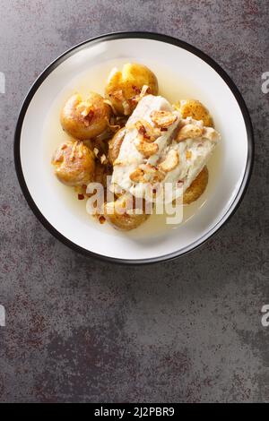 Bacalhau a Lagareiro Gegrillter gesalzener Kabeljau mit Olivenöl serviert mit gebackenen Kartoffeln in der Nähe auf dem Teller auf dem Tisch. Vertikale Draufsicht von oben Stockfoto