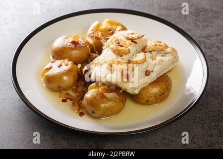 Traditioneller Bacalhau a Lagareiro Gegrillter gesalzener Kabeljau mit Olivenöl serviert mit gebackenen Kartoffeln in der Nähe auf dem Teller auf dem Tisch. Horizontal Stockfoto