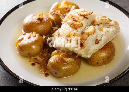 Kabeljaufilet in Olivenöl mit Knoblauch gebacken, serviert mit Kartoffeln aus der Nähe in einem Teller auf dem Tisch. Horizontal Stockfoto