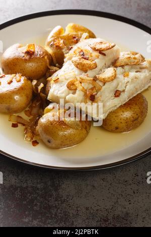 Bacalhau a Lagareiro Gegrillter gesalzener Kabeljau mit Olivenöl serviert mit gebackenen Kartoffeln in der Nähe auf dem Teller auf dem Tisch. Vertikal Stockfoto