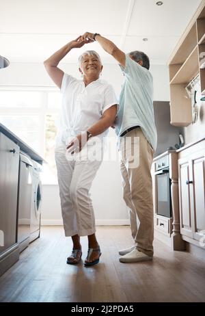 Tanz durch die Jahrzehnte. Aufnahme eines älteren Paares, das zu Hause in der Küche tanzt. Stockfoto