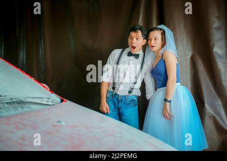 Porträt eines jungen Paares in Hochzeitskleidung, das seinen Hochzeitstag feiert. Das Paar wäscht das Auto. Lächeln, Kuss, Liebe. Stockfoto