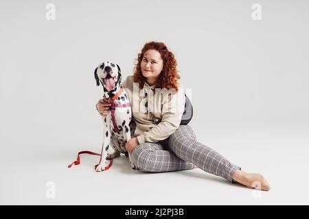 Rötliche Frau, die mit ihrem dalmatinischen Hund auf weißem Hintergrund spielt. Mensch und sein Haustier Stockfoto