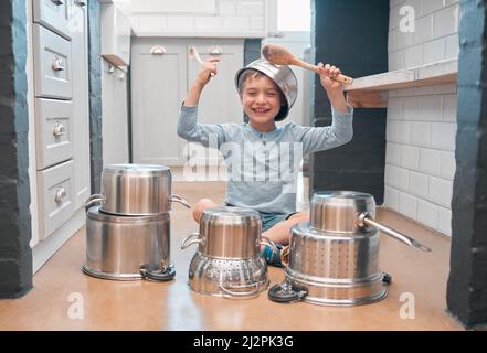 Teilen Sie Ihr Lächeln mit der Welt. Aufnahme eines entzückenden kleinen Jungen, der in der Küche mit Töpfen spielt. Stockfoto