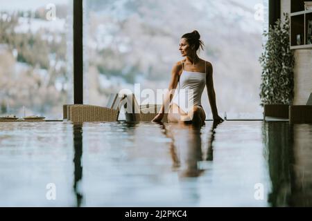 Im Winter sitzt eine attraktive junge Frau im Bikini am Pool im Hallenbad Stockfoto