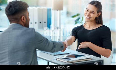 Abschluss einiger Verträge, bevor sie Mutterschaftsurlaub beginnt. Aufnahme einer Schwangeren Geschäftsfrau, die sich in einem Büro mit einem Geschäftsmann die Hände schüttelt. Stockfoto