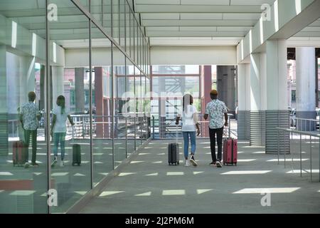 Junge schwarze Passagiere mit Koffern, die in der Nähe des Flughafens entlang der Straße laufen. Stockfoto