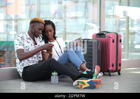 Das junge afrikanische Paar kauft die Tickets auf einem Tablet und sitzt am Bahnhof. Stockfoto