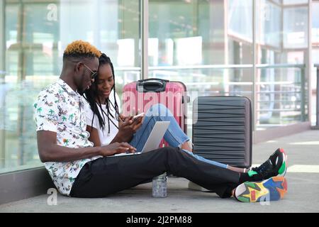 Das junge afrikanische Paar kauft seine Fahrkarten auf einem Laptop, sittin. Stockfoto