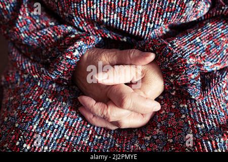 Nahaufnahme der gefalteten Hände einer nicht erkennbaren älteren Person in einem gemusterten Kleid Stockfoto