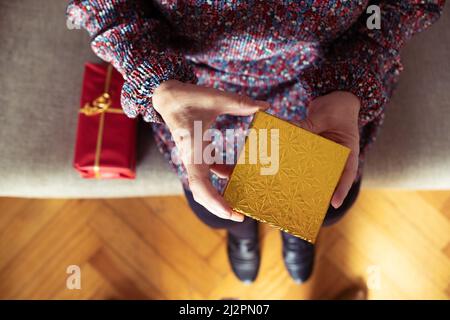 Foto von oben einer unkenntlichen Frau, die sich mit zwei Geschenken hinsetzt Stockfoto