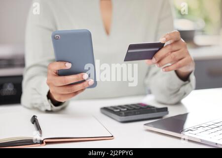 Ihr Geschäft online zu erledigen. Eine nicht erkennbare Geschäftsfrau, die ihr Mobiltelefon benutzt, während sie eine Kreditkarte im Büro hält, wurde aus dem Blickwinkel aufgenommen. Stockfoto