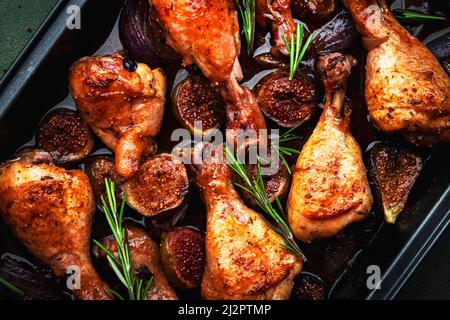 Gebackene Hähnchenbeine, Drumsticks mit süßen Feigen und Zwiebeln in balsamischer Marinade auf schwarzem Backblech, rostiger grüner Tischhintergrund, Draufsicht Stockfoto