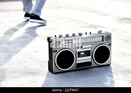 Der Klang der Musik. Hochwinkelige Aufnahme einer Boombox auf dem Boden mit einer nicht erkennbaren Tänzerin im Hintergrund. Stockfoto