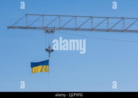 Helsinki / Finnland - 3. APRIL 2022: Die Flagge der Ukraine winkt im Wind auf einem Baukran-Boom. Stockfoto