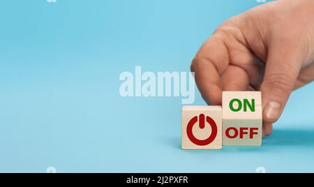 Hand dreht einen Würfel und ändert das Wort aus auf ein. Schalter auf einem Holzwürfel mit Inschriften an und aus Wort auf blauem Hintergrund. Start-Stopp Stockfoto