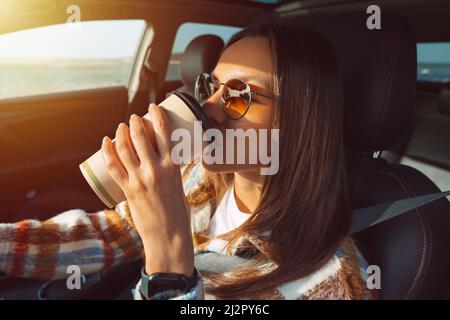Junge schöne Frau, die ein Auto fährt und Kaffee trinkt. Stockfoto